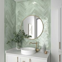 a bathroom with green tiles on the wall and a round mirror over the sink in front of it