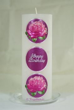 a white candle with pink roses on it and the words happy birthday written in purple