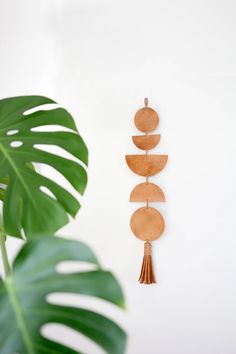 a wall hanging with wooden discs and tassels on it next to a plant