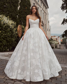 a woman in a white wedding dress standing on a cobblestone street