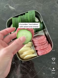 a person is holding a pickle in a container with sliced vegetables and meats