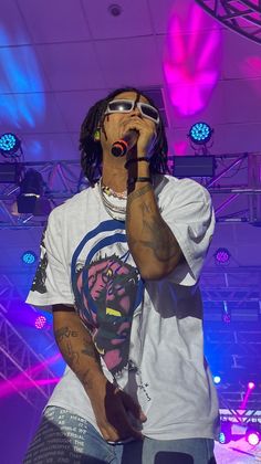 a man standing on top of a stage holding a microphone in his hand and wearing sunglasses