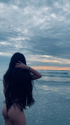 a woman standing on top of a beach next to the ocean with her arms behind her head