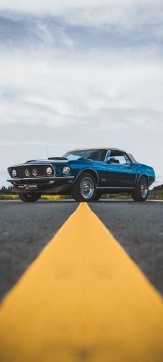 an old blue car is parked on the side of the road next to a yellow arrow