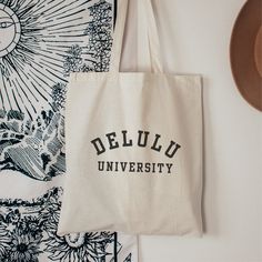 "DELULU UNIVERSITY TOTE BAG  Gift yourself or your delulu friends with this funny tote bag. This 100% cotton bag is 15\" x 16\" and perfect for everyday use.  Designed to tote your essentials, this tote bag features sturdy 20\" handles (made from the same canvas), making it easy to carry.  Designed with an appreciation for a minimal aesthetic, it will compliment any outfit.  Must have accessory for a day at the beach, to carry your school books or to run your daily errands. 🦋100% cotton canvas Minimalist Tote Bag Design, Tote Bag Design Aesthetic, Custom Tote Bag Aesthetic, Delulu Aesthetic, Tote Bag Design Ideas Aesthetic, Toat Bag, Cool Tote Bag Design, Aesthetic Tote Bag Design, Cute Tote Bag Design