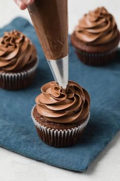 a chocolate cupcake being frosted with icing on a blue napkin next to other cupcakes