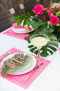 the table is set with pink and white place mats, plates, silverware, and flowers