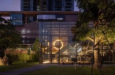 the entrance to an office building lit up at night with trees and bushes in front