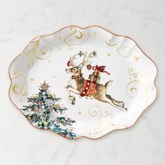 a white and gold christmas plate with a reindeer on it's back holding a present