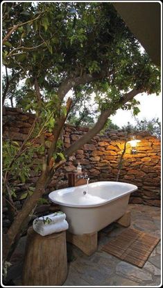 a white bath tub sitting under a tree next to a stone wall and wooden stumps