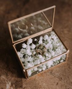 two wedding rings sitting in a box filled with white flowers on top of a table