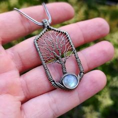 a person holding a tree of life pendant with a rainbow stone in it's center