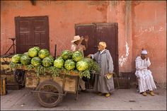 an old man pushing a cart full of watermelon in front of a pink building