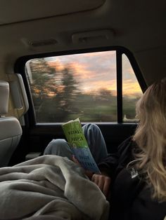 a woman sitting in the back seat of a car reading a book while looking out the window