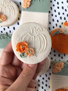 a hand holding a small white button with flowers and pumpkins in the background on a polka dot tablecloth