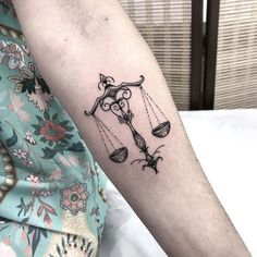 a woman's arm with a tattoo on it that has an image of a scale and flowers