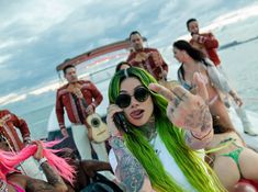 a group of people sitting on top of a boat with green hair and tattoos in front of them