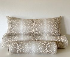 two pillows sitting next to each other on top of a white table with a brown and white pillow