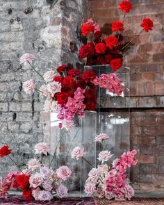 red and pink flowers are in clear vases on a rug next to a brick wall