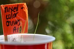 an orange sign is stuck to the side of a red cup with grass sticking out of it