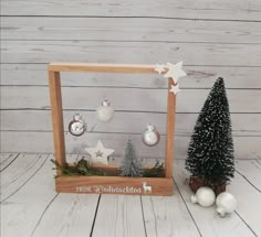 a wooden frame with ornaments and a small christmas tree in it on a white wood floor