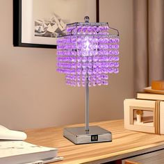 a purple lamp sitting on top of a wooden table next to a book and pictures