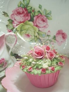 a pink cupcake sitting on top of a plate next to a teacup and saucer