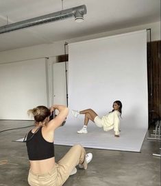 two women sitting on the ground in front of a white backdrop and one woman standing up