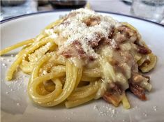 a white plate topped with pasta covered in grated cheese and meat sauce on top of it