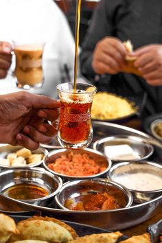 people are serving themselves food from trays on a table with cups and saucers