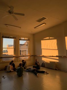 four people sitting on the floor in an empty room with windows and fan above them