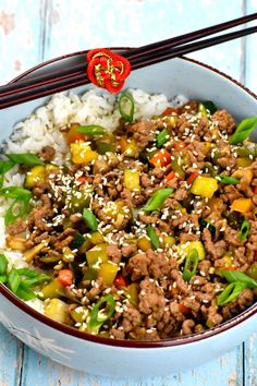 a bowl filled with meat and vegetables on top of rice next to chopsticks