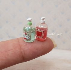 two miniature bottles sitting on top of a persons finger, one is red and the other is green