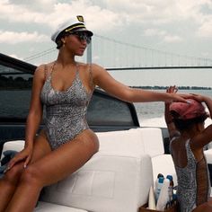 two women sitting on the back of a boat, one in a silver bathing suit