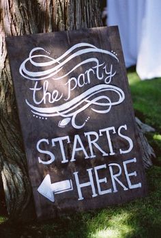 a sign that says the party starts here next to a tree with red lettering on it