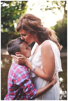 a woman kissing a boy in front of water