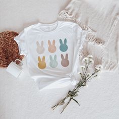 a t - shirt with bunny ears on it next to some flowers and a straw hat