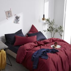 a bed with red and blue sheets in a white room next to a potted plant