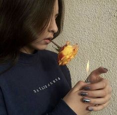 a woman holding a rose in her right hand and looking down at it with both hands