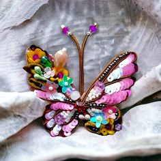 a colorful butterfly brooch sitting on top of a white piece of cloth covered in buttons