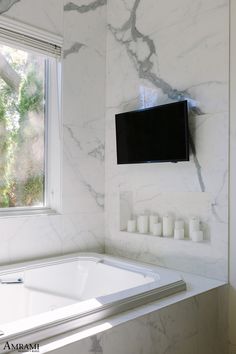 a white bath tub sitting next to a tv mounted on the side of a wall