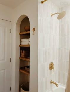 a bathroom with white tile and gold fixtures in the shower area, next to a bathtub