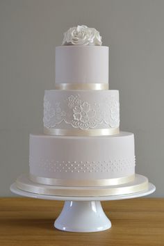 a three tiered wedding cake with white flowers and lace on the top, sitting on a wooden table