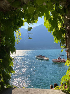 two boats floating on top of a large body of water next to a lush green forest covered hillside