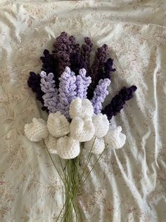 crocheted lavenders and lavender flowers on a bed with white sheets in the background