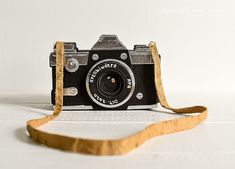 an old fashioned camera sitting on top of a white table next to a brown strap