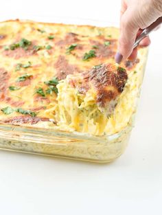 a hand holding a piece of broccoli casserole in a glass dish