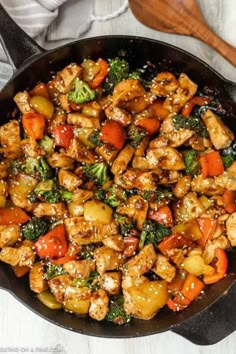 chicken and vegetable stir fry in a skillet with wooden spoons on the side