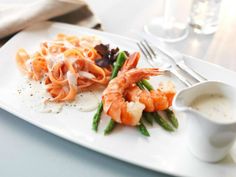 a white plate topped with pasta and shrimp next to a glass of water on a table