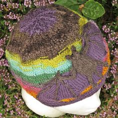 a knitted hat on top of a white mannequin head in front of purple flowers